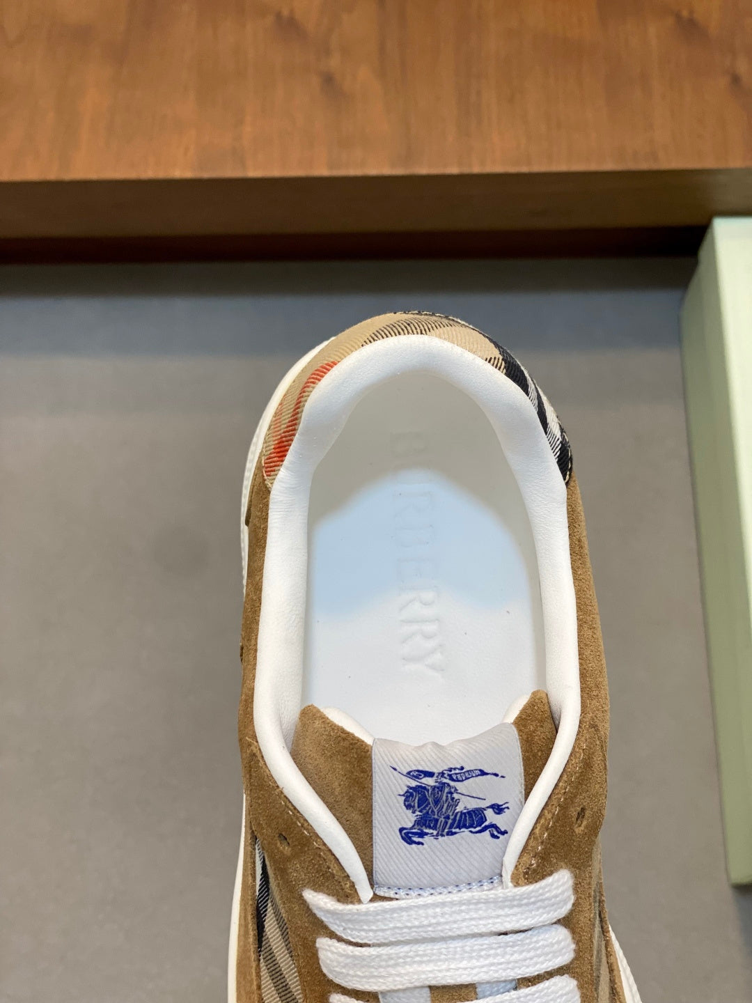 Sneaker heel view with tan suede, white lining, and blue logo print