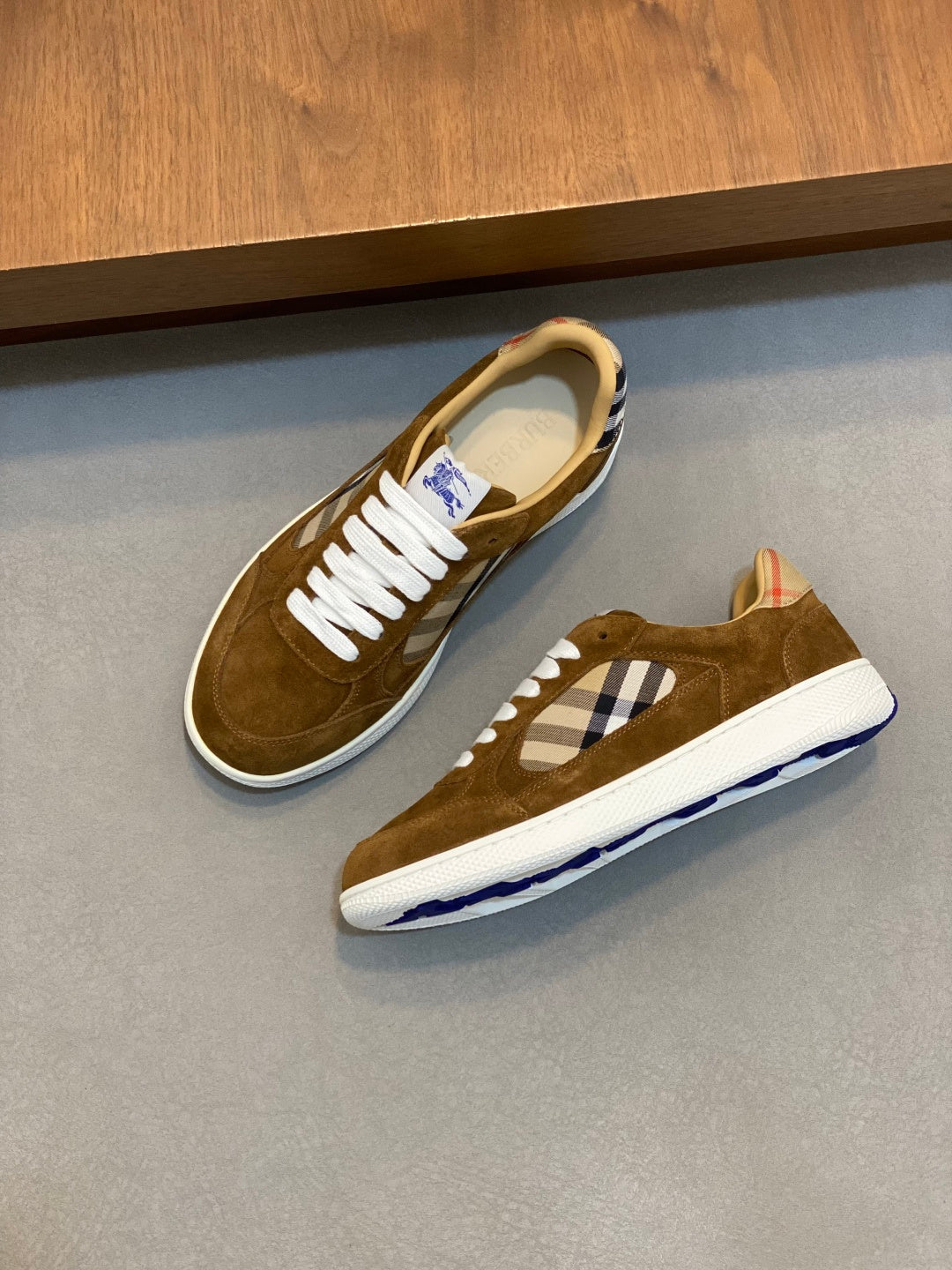 Pair of brown suede low-top sneakers with white laces and blue check panel on the sides