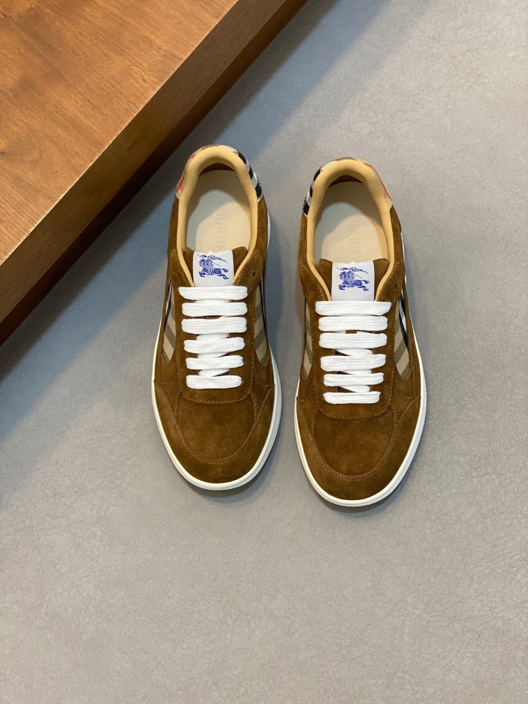 Brown suede low-top sneakers with white laces and blue check detail near the tongue