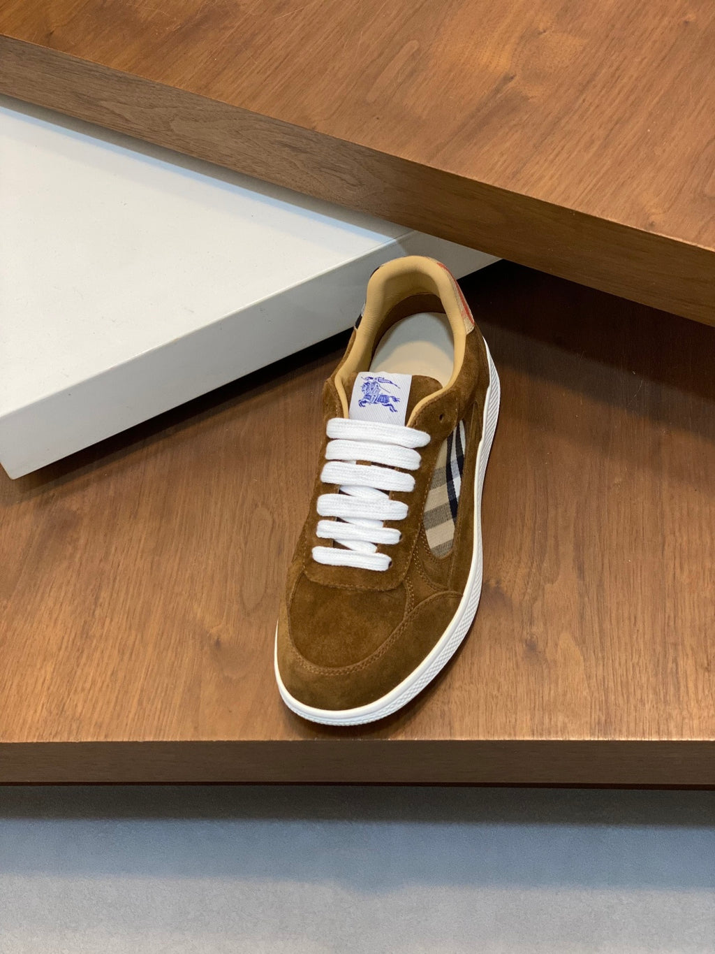 Single brown suede low-top sneaker on shelf, featuring white laces and check detail