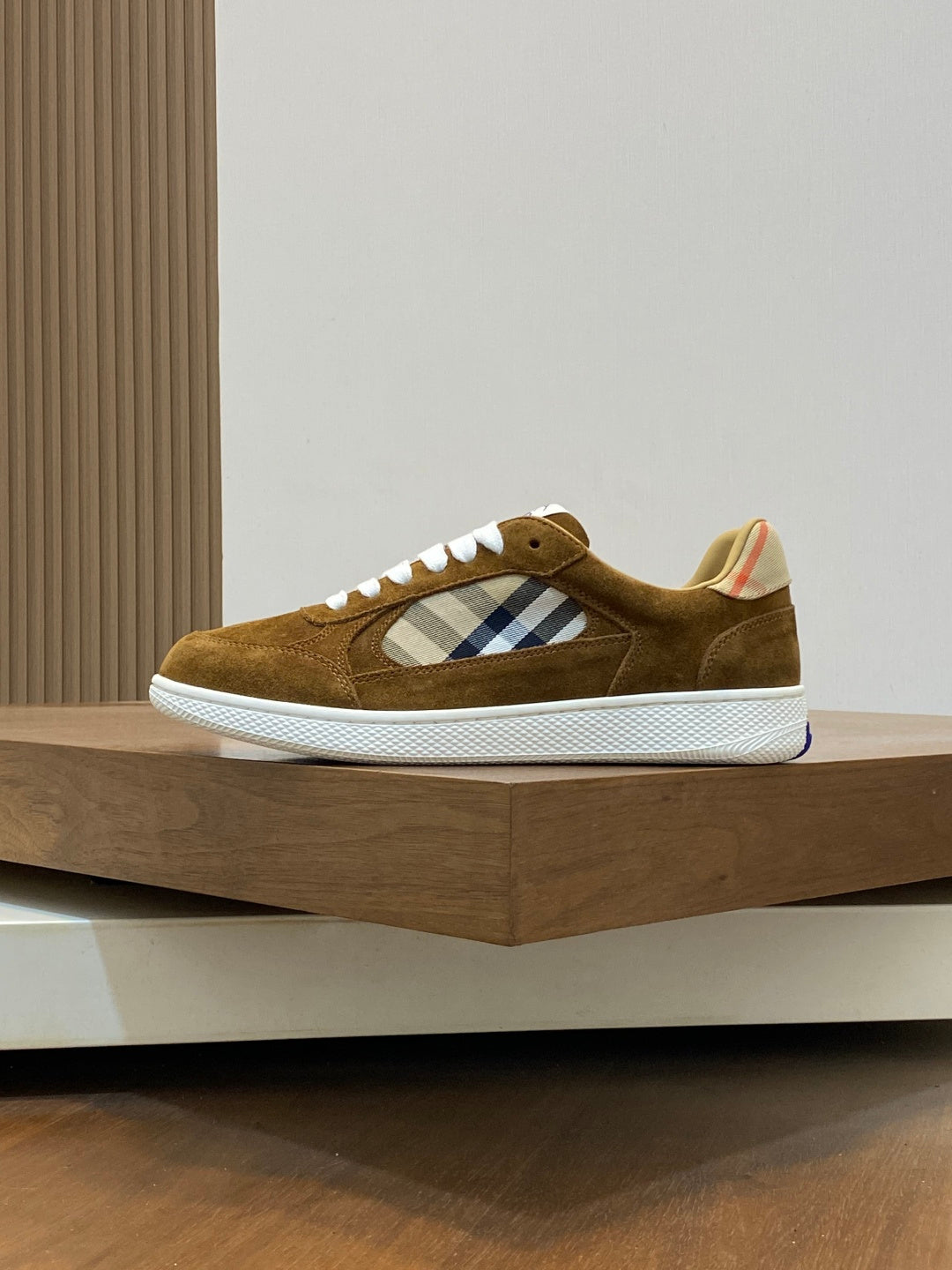 Brown suede low-top sneaker side view with blue-and-white check patch and white rubber sole