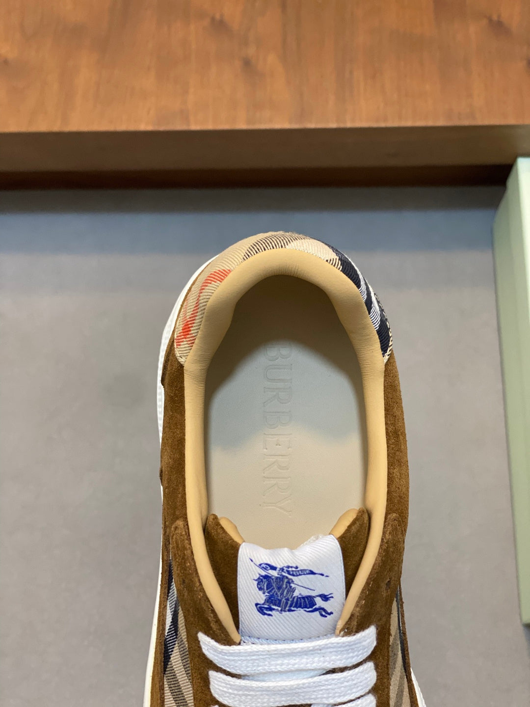 Close-up of brown suede sneaker tongue with blue logo print and white laces