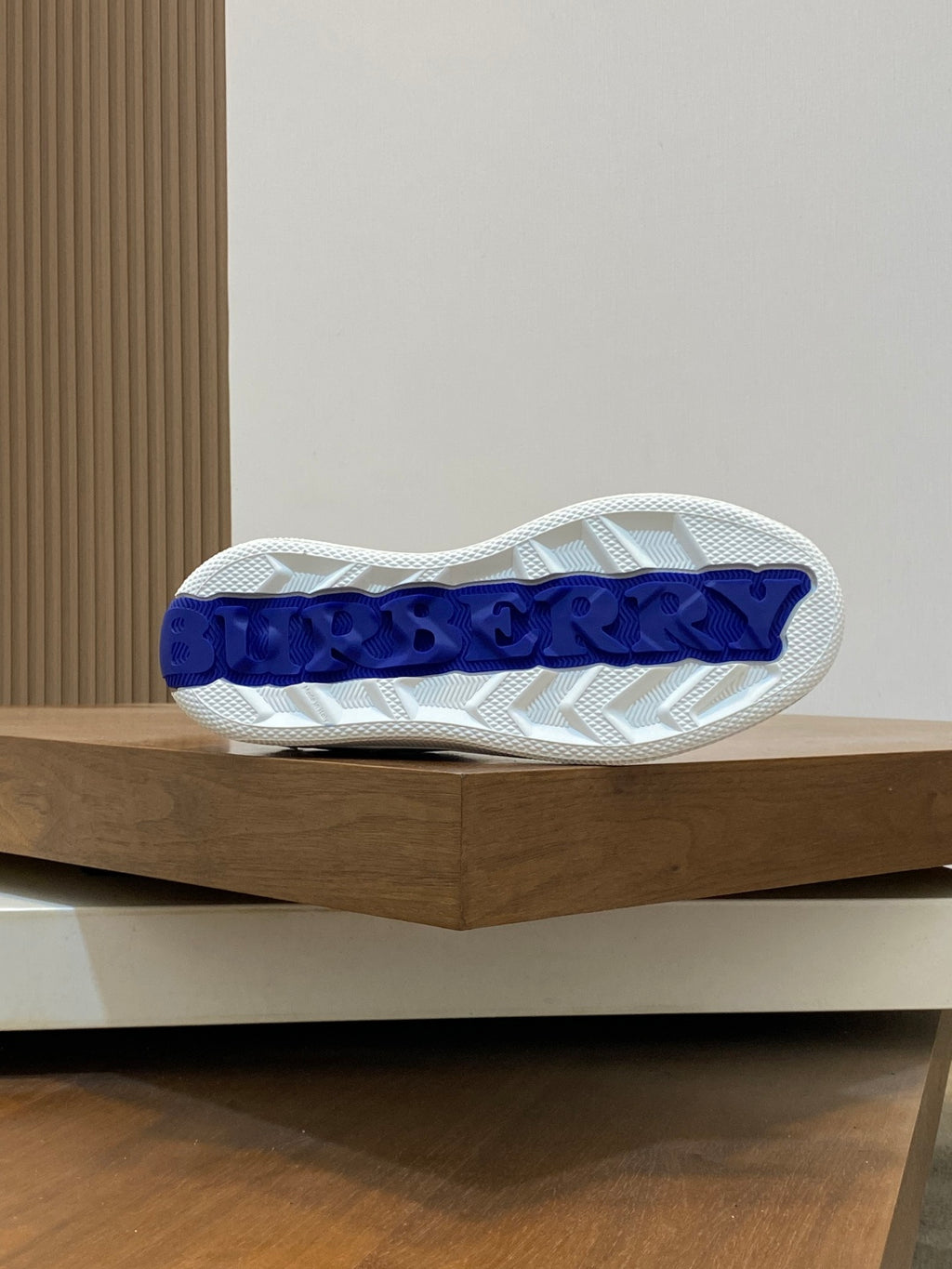 White sneaker outsole with blue Burberry lettering and textured tread.