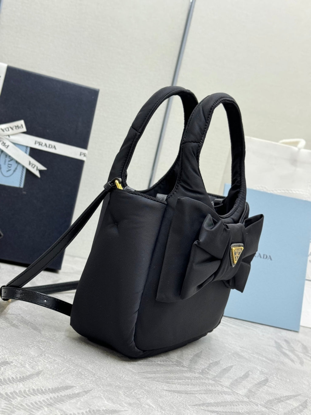 Prada black nylon mini bag with two handles, bow front, and gold logo plaque