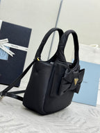 Prada black nylon mini bag with two handles, bow front, and gold logo plaque