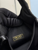 Prada black nylon mini bag close-up of gold logo patch and textured fabric