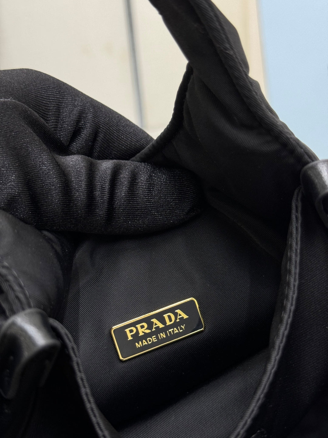 Prada black nylon mini bag close-up of gold logo patch and textured fabric