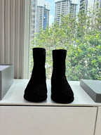 Black suede ankle boots, pair standing on a white display ledge