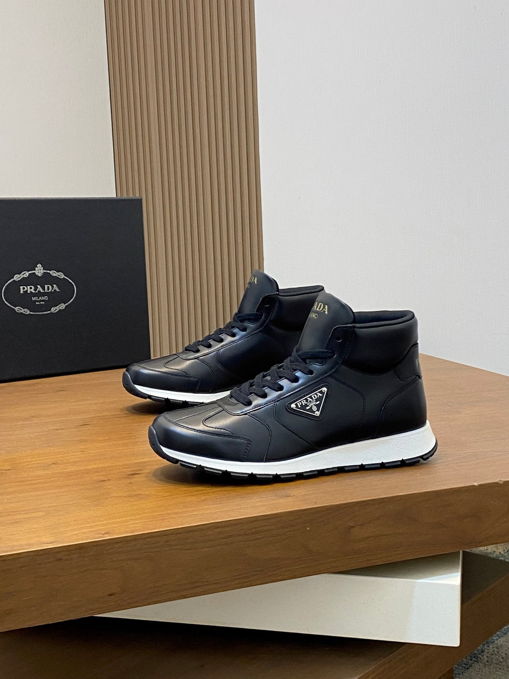 Prada dark leather sneakers, angled side view with lace-up and logo patch.