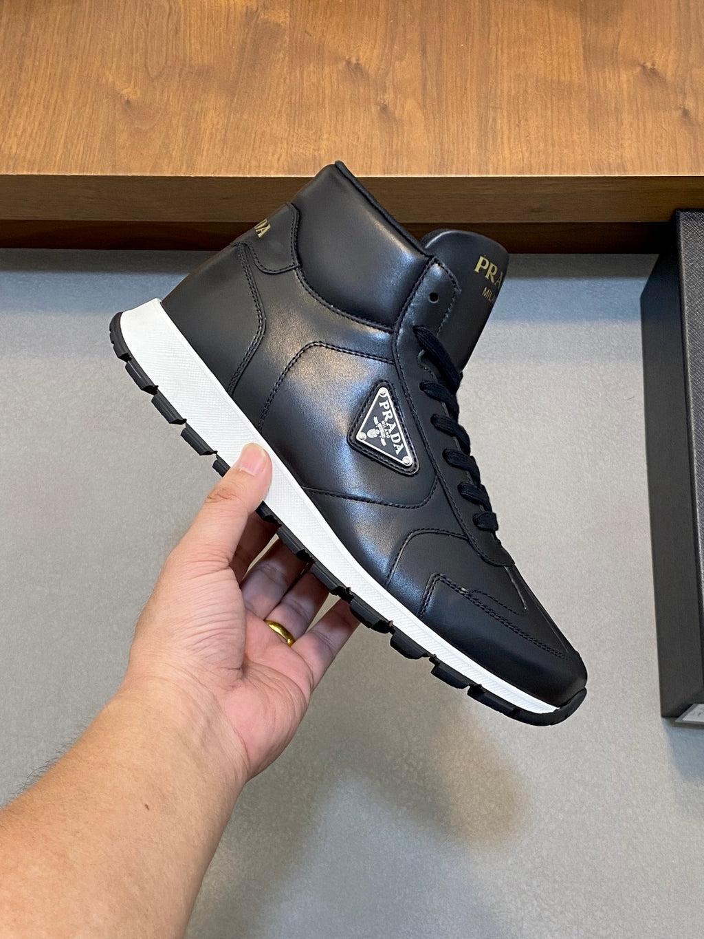 Prada dark leather high-top sneakers with lace-up, held in hand for viewing.