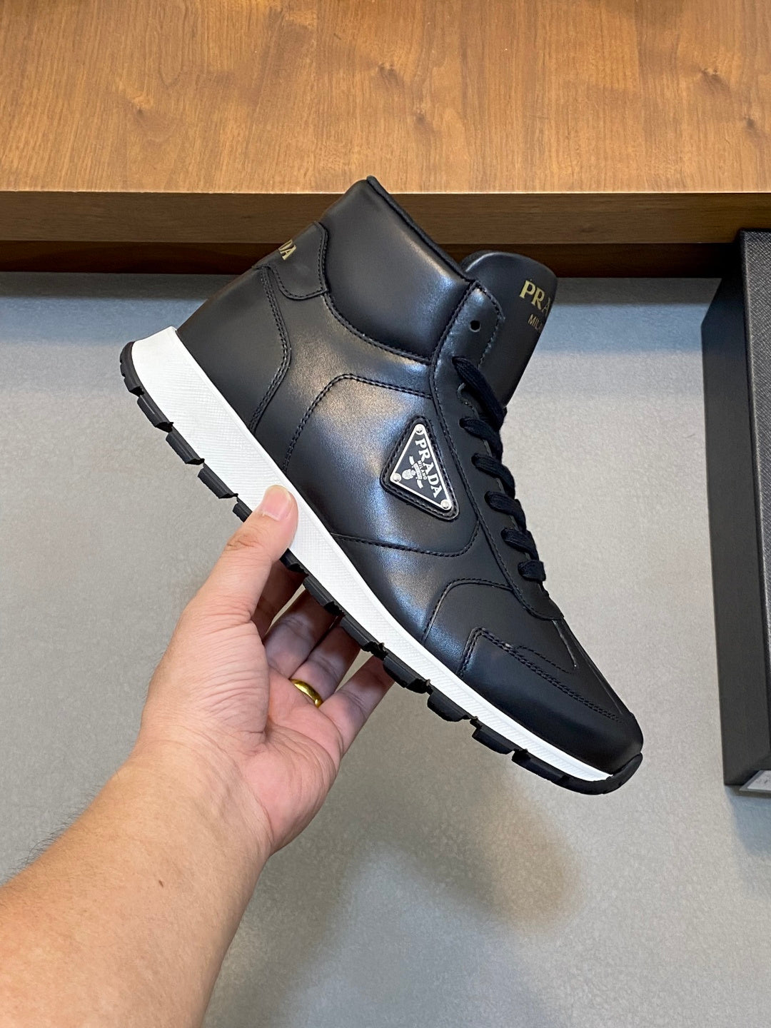 Prada dark leather high-top sneakers with lace-up, held in hand for viewing.