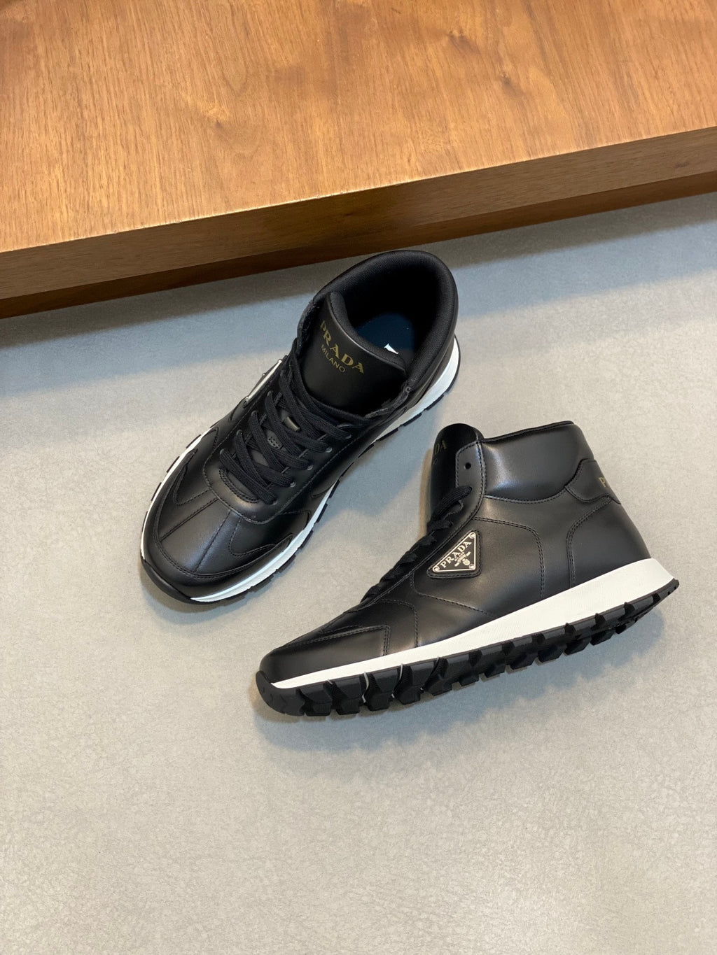 Prada dark leather sneakers, one shoe side view with textured sole tread.