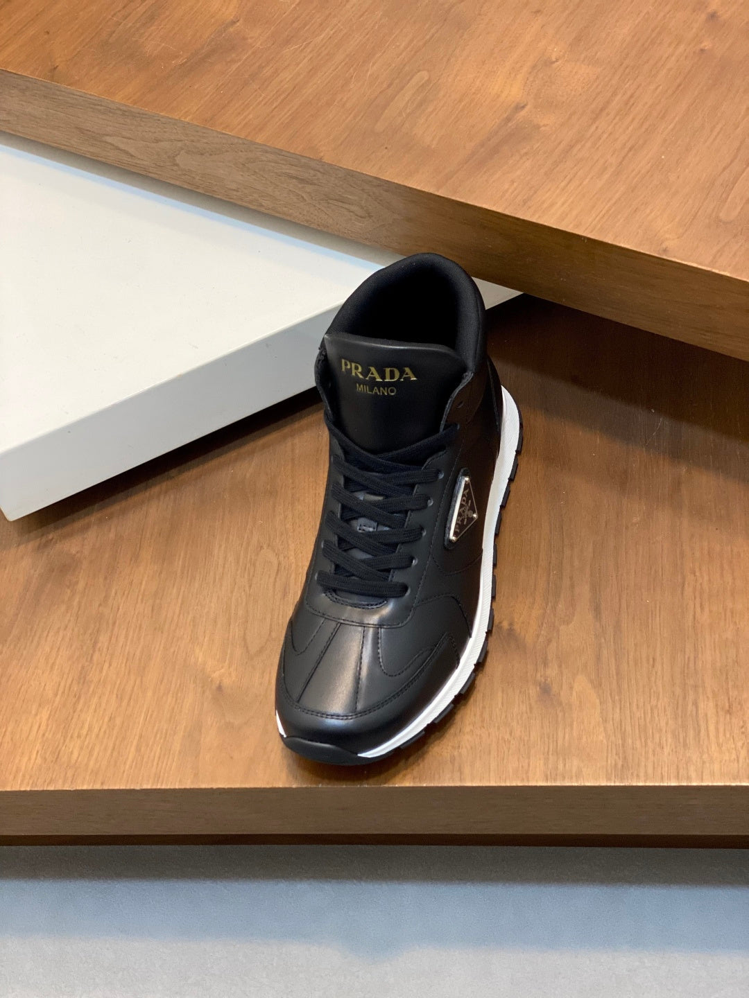 Prada dark leather sneakers, front view with lace-up and logo on tongue.
