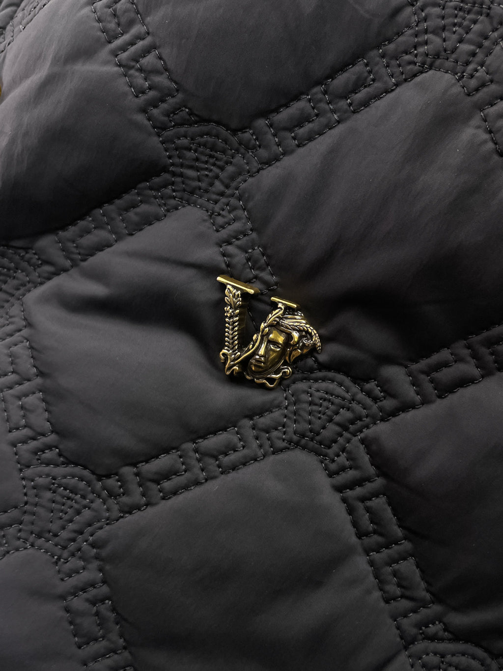 Versace quilted jacket fabric detail with gold crest emblem on chest pocket