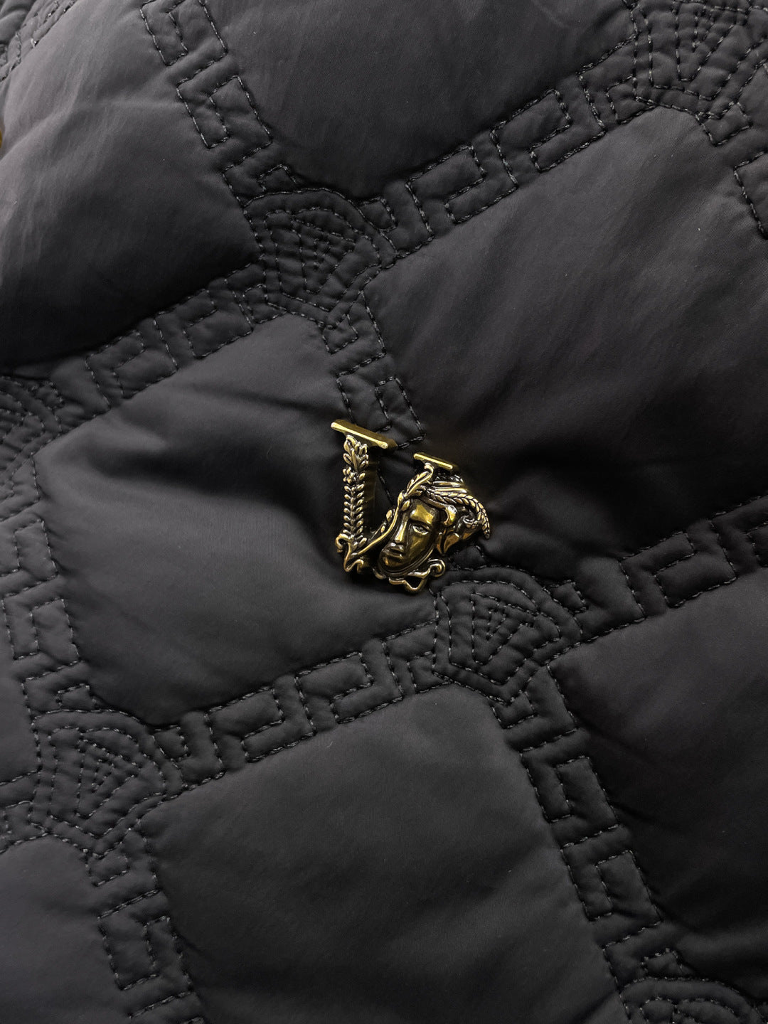 Versace quilted jacket fabric detail with gold crest emblem on chest pocket