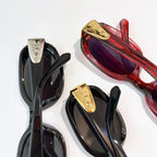 Sunglasses close-up: black frames with gold-tone logo detail and dark lenses