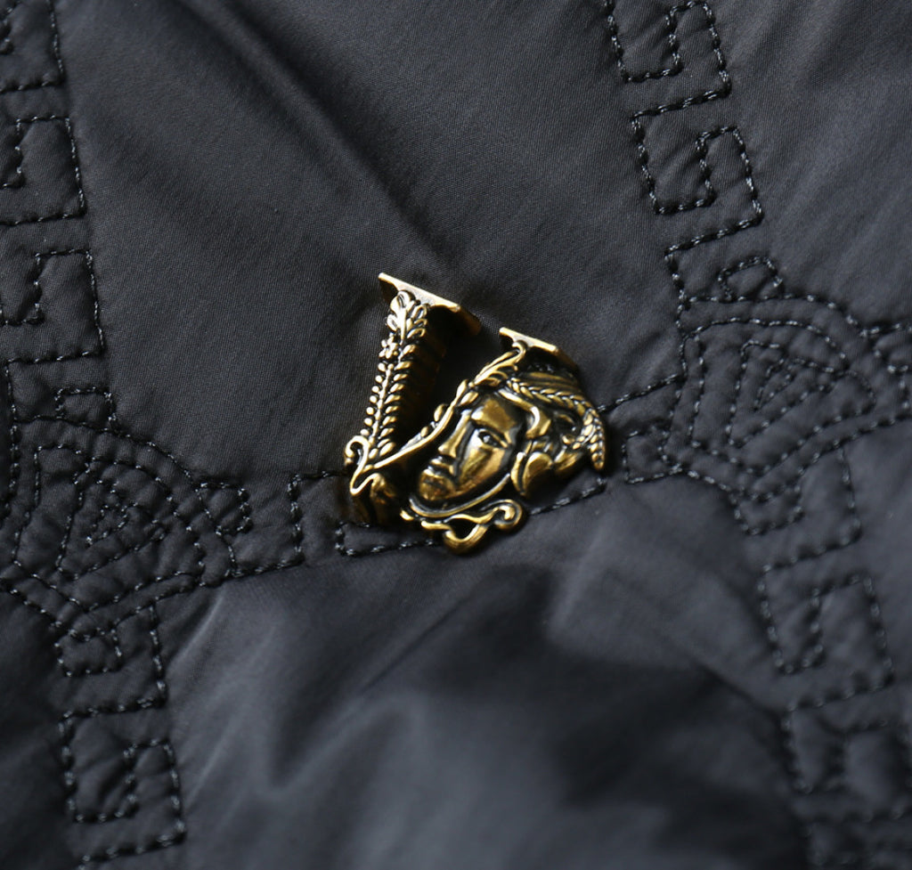 Black quilted jacket emblem patch detail with gold-toned logo