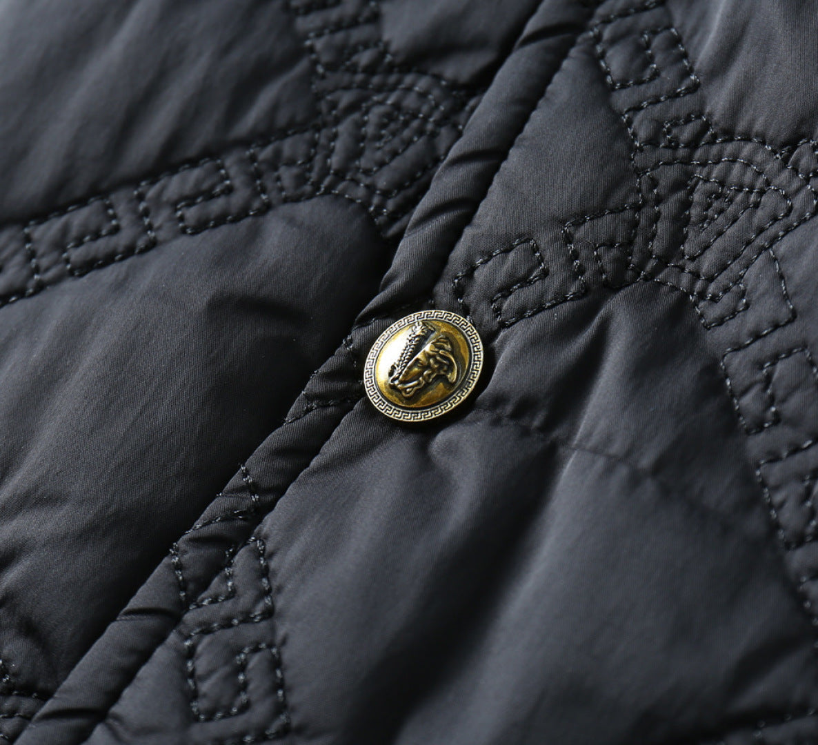 Black quilted fabric with gold emblem button detail and dark stitching