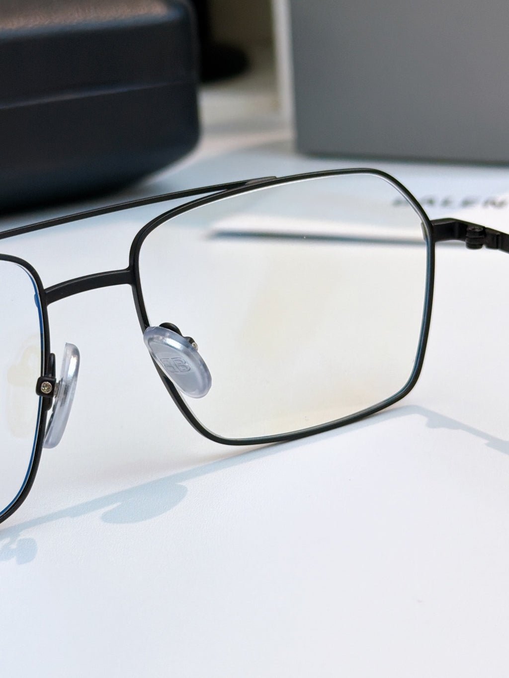 Black eyeglasses close-up with oval lens and metal bridge detail.