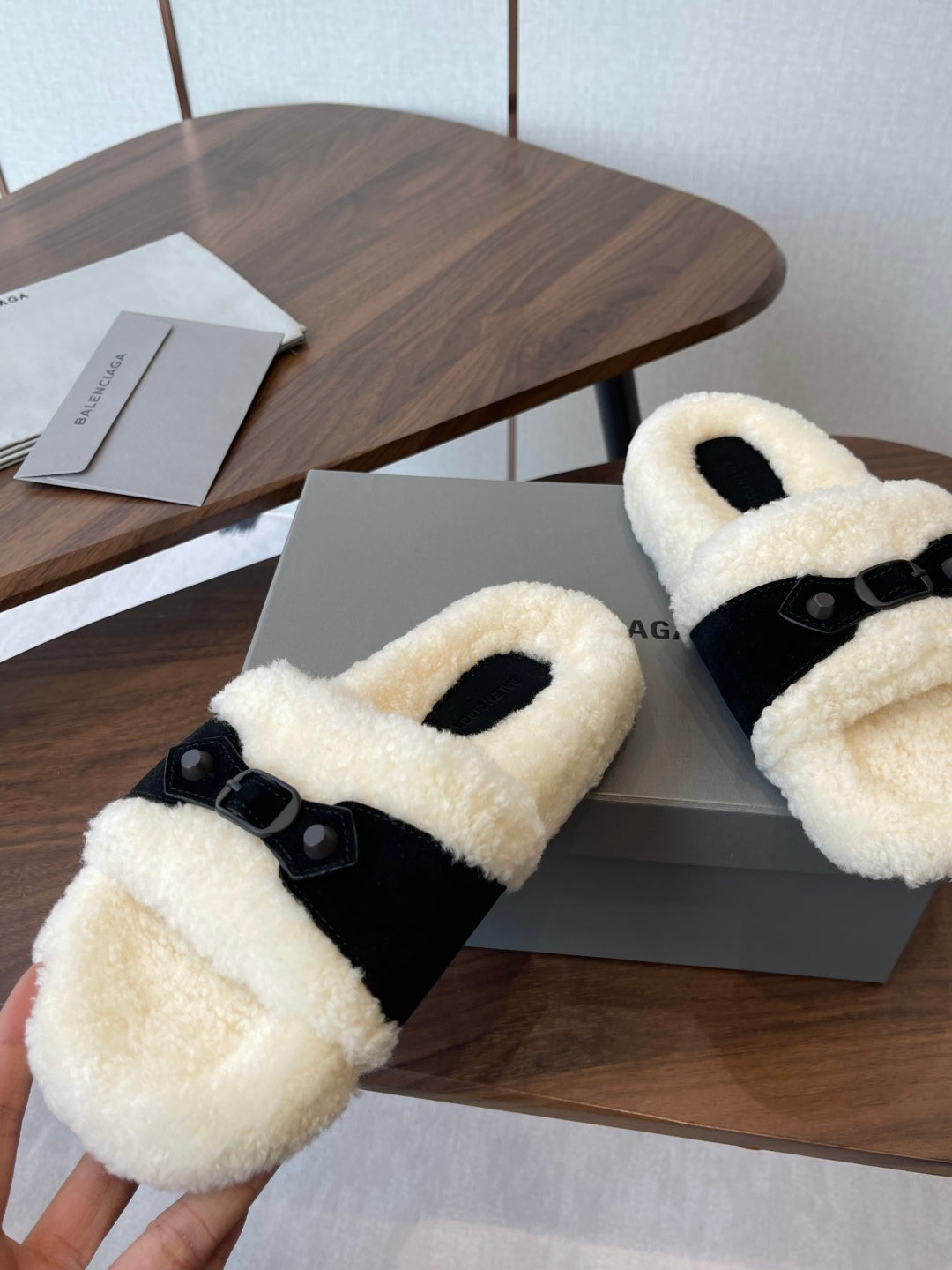 Balenciaga shearling slide sandals with black strap and cream fluffy footbed, angled on box