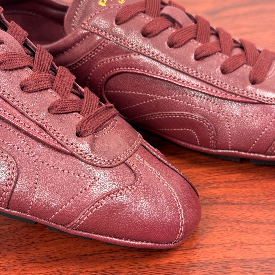 Prada unisex leather sneaker close-up in burgundy, laces and stitched toe cap