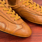 Tan sneakers close-up with yellow laces and embossed logo on the side panel