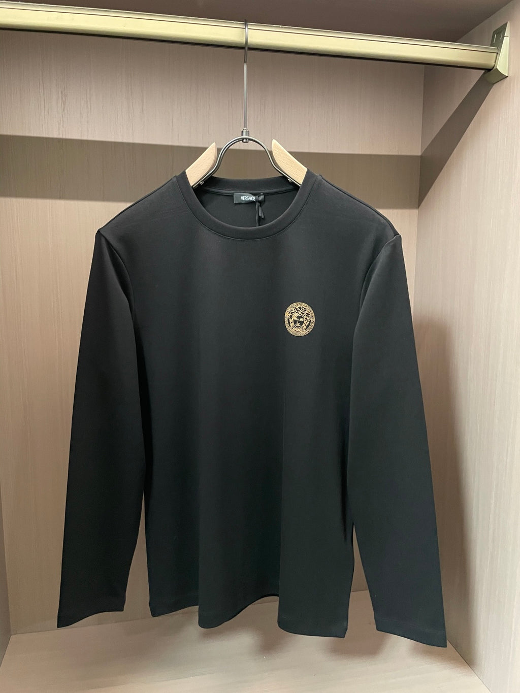 Black long-sleeve crewneck shirt with gold Medusa-style emblem on chest