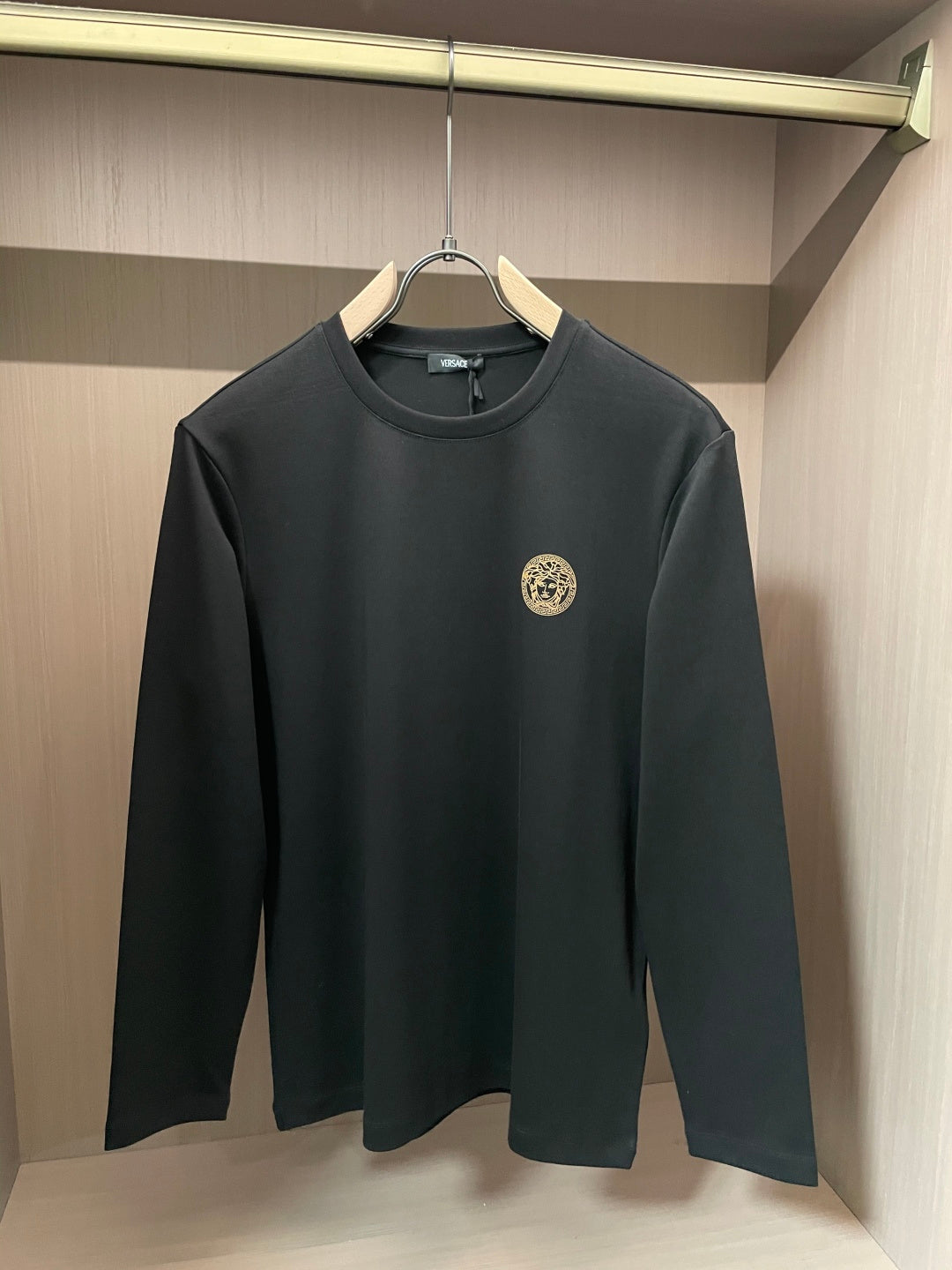 Black long-sleeve crewneck shirt with gold Medusa-style emblem on chest