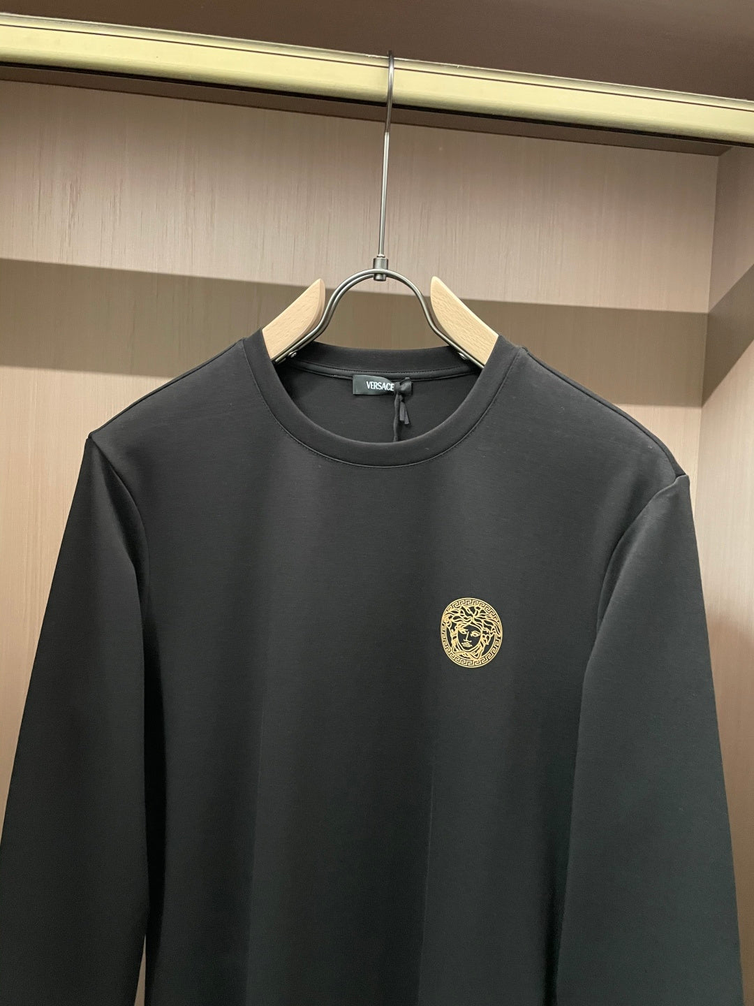 Black long-sleeve crewneck shirt with chest logo patch and small neckline tag
