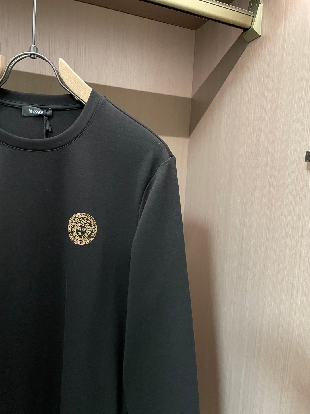 Black long-sleeve crewneck shirt with gold emblem close-up on left chest