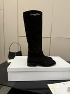 Single black knee-high suede boot on a white box, rounded toe and block heel