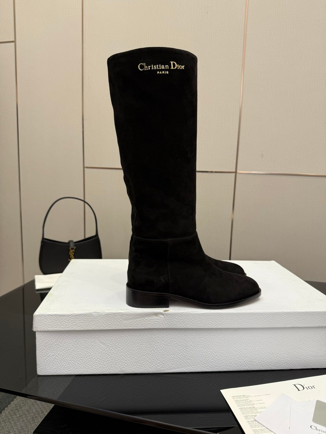 Single black knee-high suede boot on a white box, rounded toe and block heel