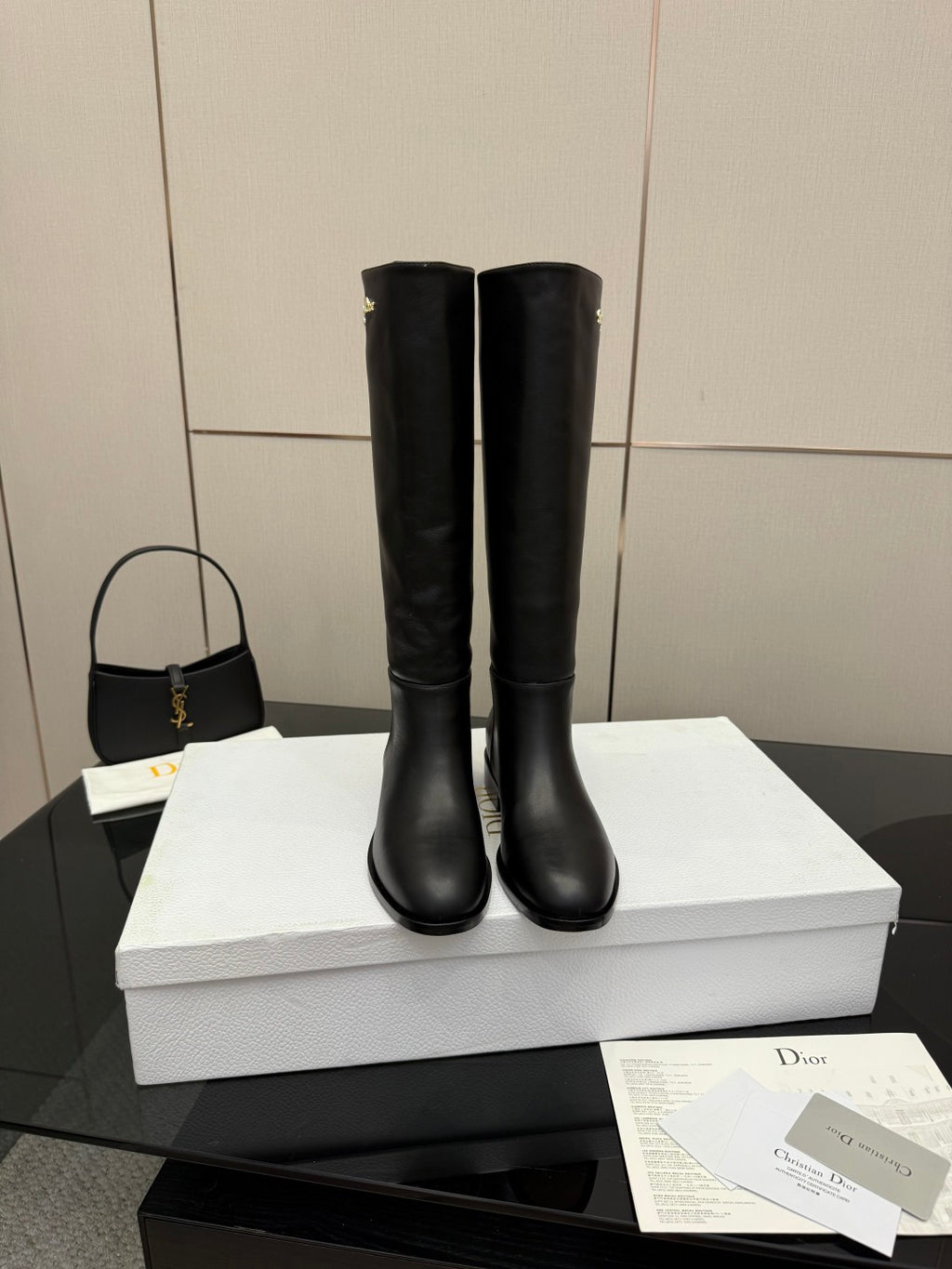 Black leather knee-high boots standing on white shoebox, rounded toe