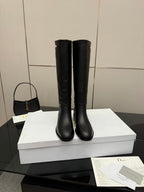 Black leather knee-high boots standing on white shoebox, rounded toe