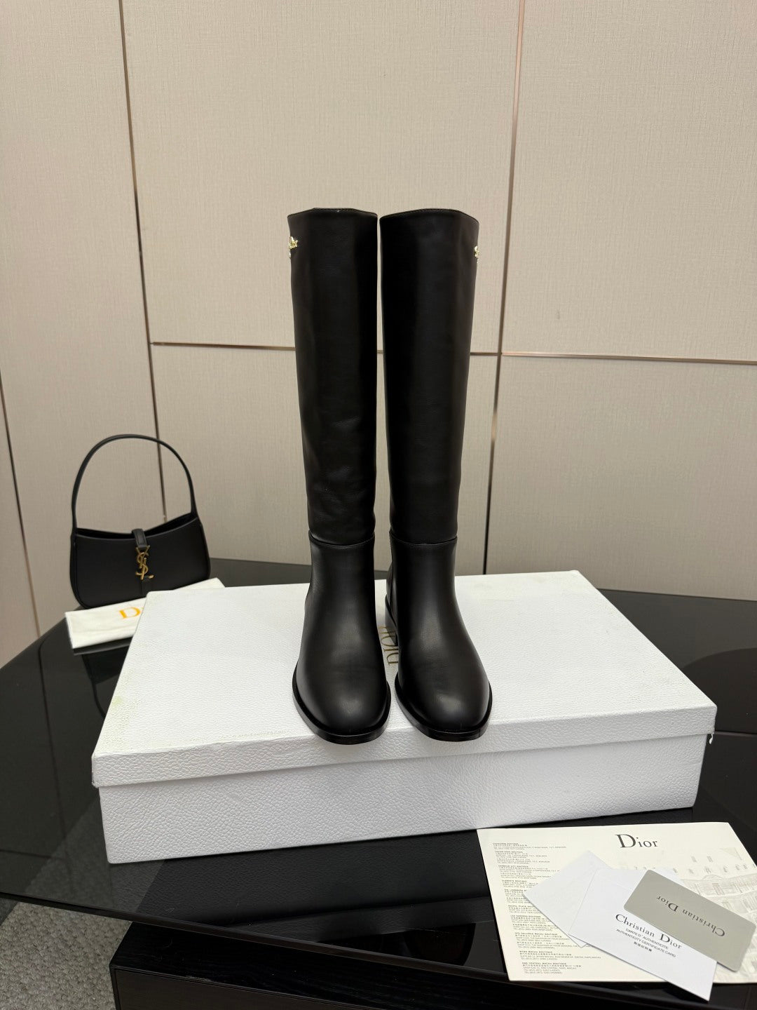 Black leather knee-high boots standing on white shoebox, rounded toe