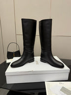 Black leather knee-high boots with low heel, stacked on shoebox