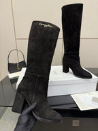 Black knee-high suede boots on display; hand holds one boot on the box