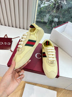 Women's yellow low-top sneakers, hand holding shoe with Web stripe detail