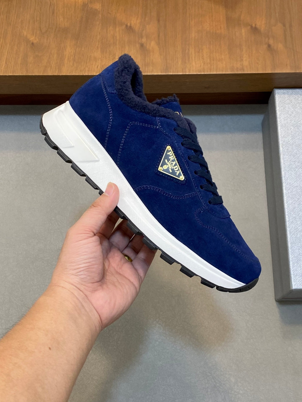 Prada unisex suede sneaker in dark blue held in hand, gold logo on side