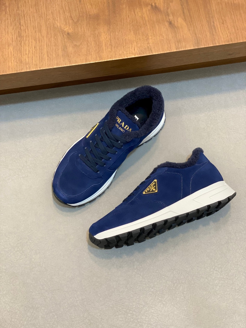 Prada unisex suede sneakers in dark blue, angled top view with gold triangle logo
