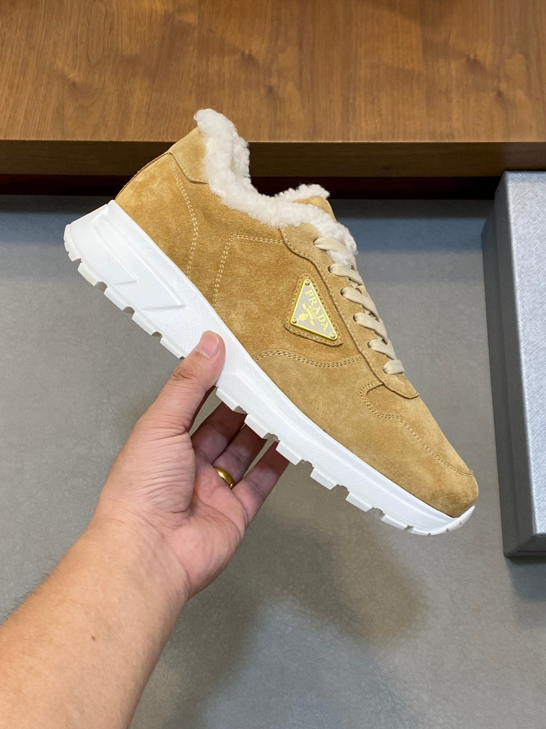 Prada unisex tan suede sneaker held in hand, showing shearling collar and white sole