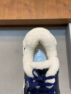 Prada unisex sneaker close-up: plush sherpa collar, blue laces, triangular logo patch.