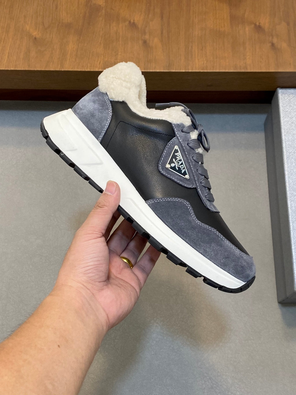 Prada unisex sneakers held in hand; dark gray upper with shearling collar and sole
