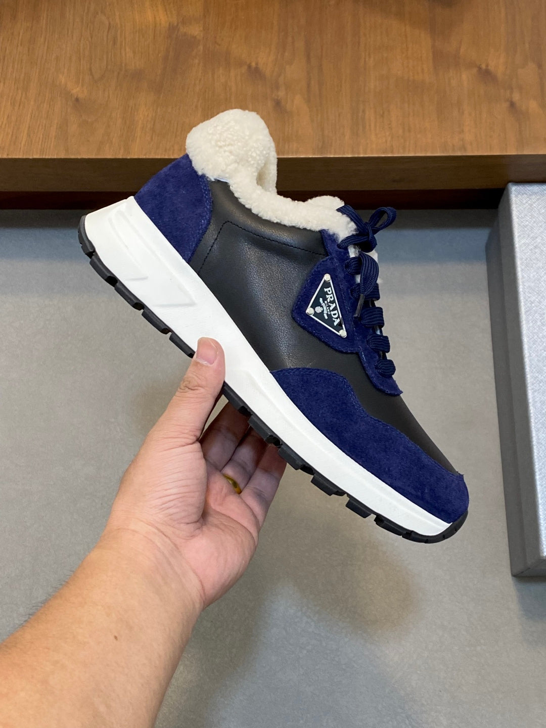 Hand holding Prada unisex sneaker: dark blue suede with plush collar, white sole.