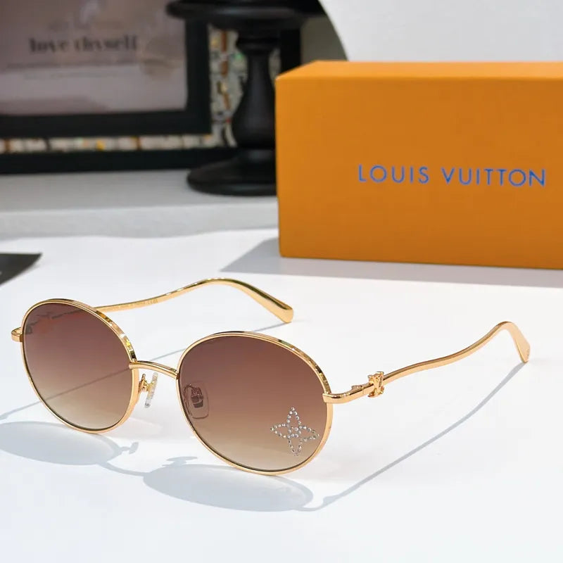 Round sunglasses with gold frame and tinted brown lenses, rhinestone logo detail.