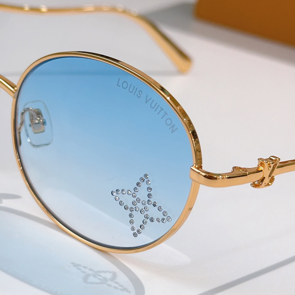 Round sunglasses close-up with gold rim and light blue gradient lens, rhinestone detail