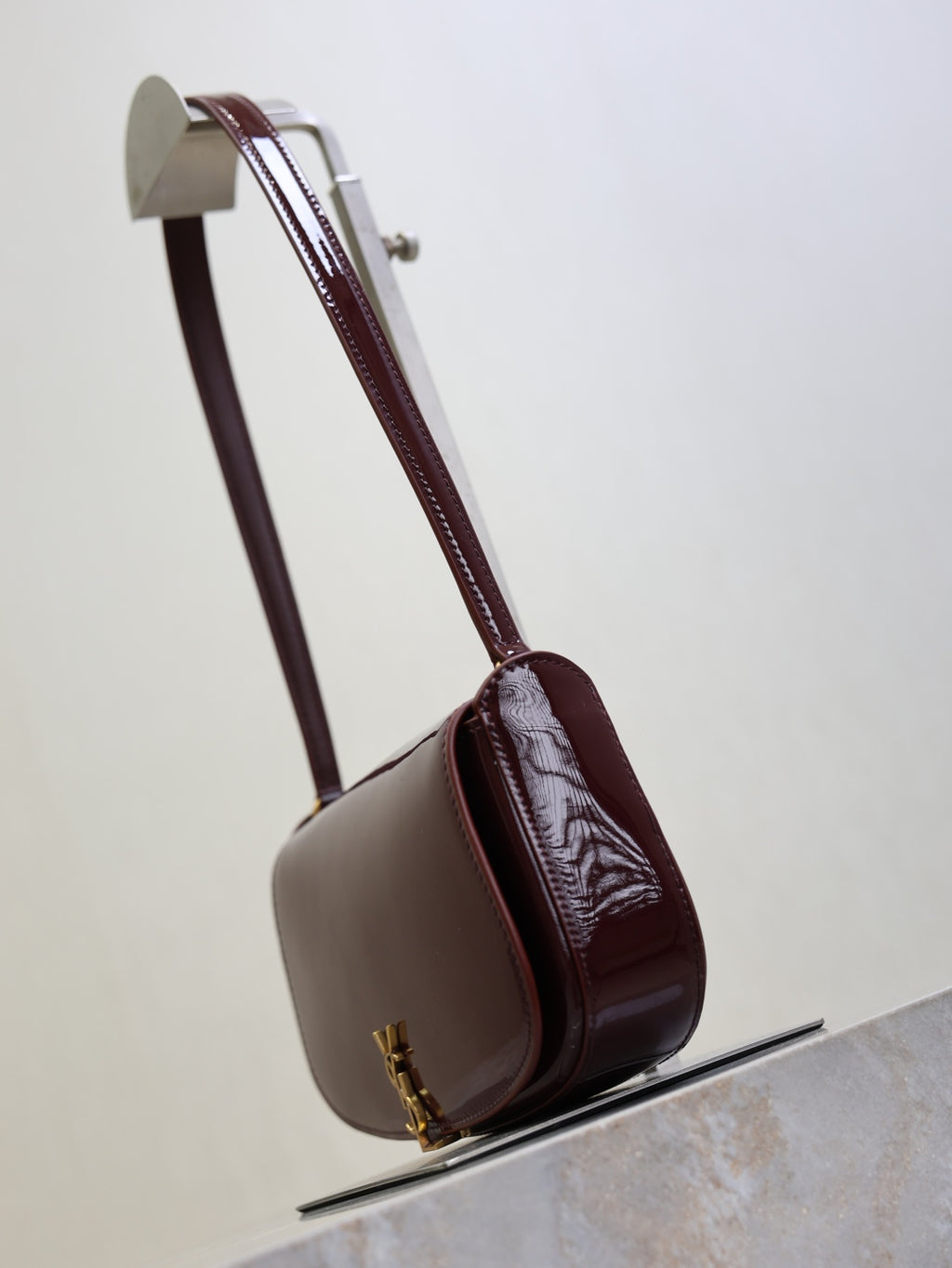 Mini shoulder bag with burgundy strap, rounded body, gold clasp at base