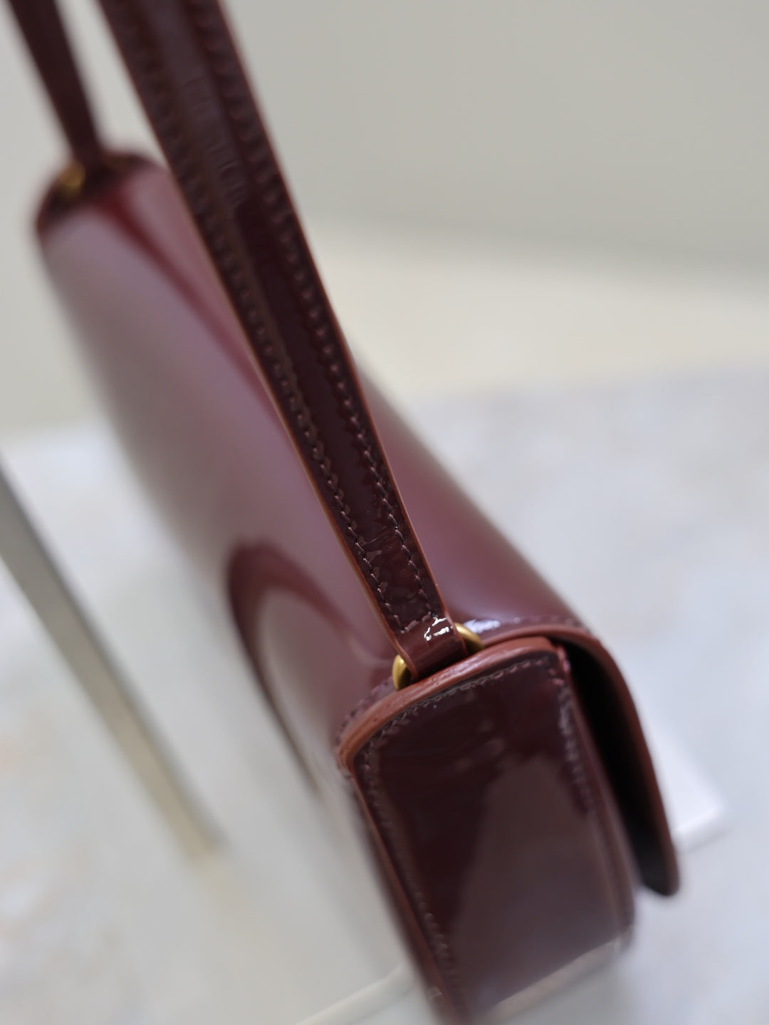 Mini shoulder bag strap and flap close-up, burgundy leather and gold-tone accents