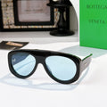 Black oversized sunglasses with blue mirrored lenses and green-accent temples.