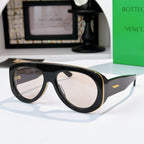 Black oversized sunglasses with light reflective lenses and green-accent temples.